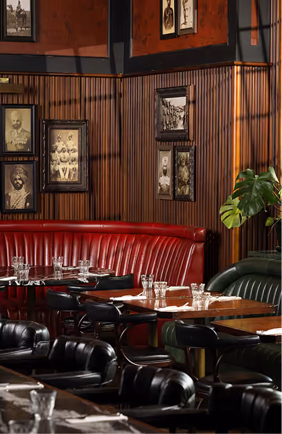 Red leather banquette and dark green booths below framed vintage portraits at Doolally
