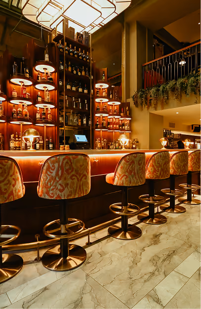 Patterned bar stools along a brass-trimmed bar and backlit spirits shelves at The Stapleton