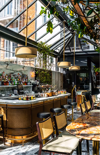 Brass-clad bar and drum pendant lights under the glass atrium roof at The Grayson