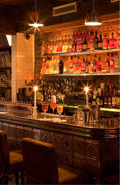 Vintage Cocktail Club bar with shelves of colourful spirits, cocktails and warm ambient lighting.