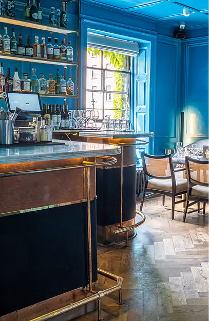 Brass-trimmed bar and spirit shelves against turquoise walls at The Grayson