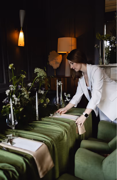 Staff member setting a green-draped private dining table with candles and white florals at The Grayson