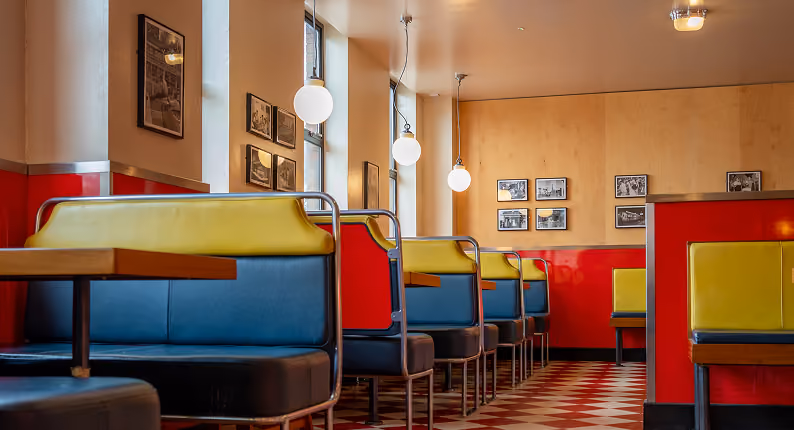 Retro diner booths in red, blue and yellow above a chequerboard floor at Wowburger