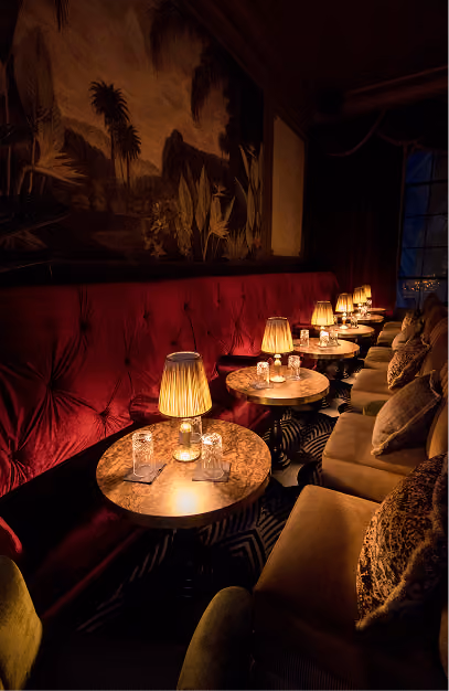 Stella Cocktail Club with red velvet seating, marble tables, warm table lamps and tropical wall artwork.