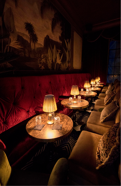Stella Cocktail Club with red velvet seating, marble tables, warm table lamps and tropical wall artwork.