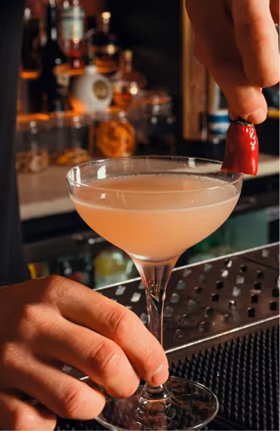 Bartender garnishing a pale pink coupe cocktail with a red chilli at Angelina's