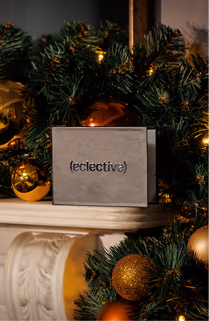 Eclective gift box on a mantelpiece framed by a lit Christmas garland and gold baubles