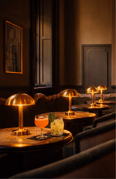 Brass dome table lamps and cocktails along a curved banquette in a low-lit private bar