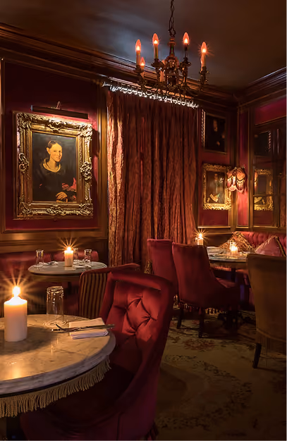 Red velvet chairs and gilt-framed portraits in the candlelit dining room at Peruke & Periwig