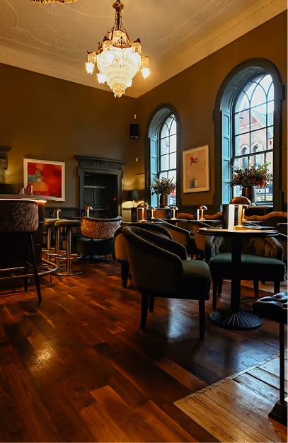 Crystal chandelier and arched windows above green velvet seating in the bar at The Stapleton