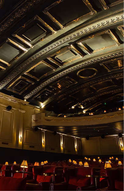 Ornate gilded ceiling above red velvet armchairs and lamp-lit tables at Stella Cinema