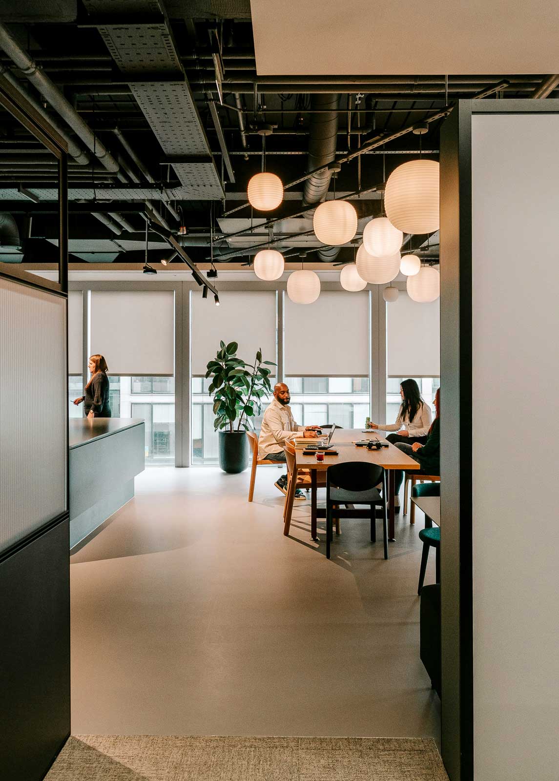 Modern office space with people working at a table under hanging round light fixtures.