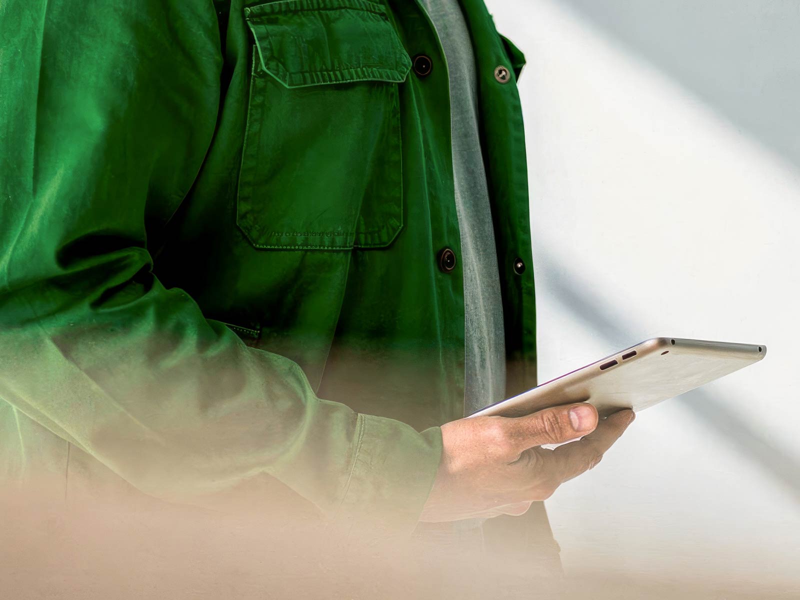 Person in green jacket holding and using a tablet device with a white background.