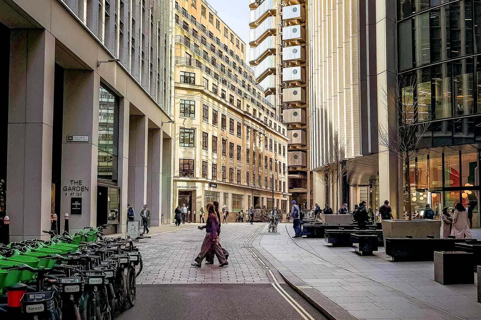 Urban London City street scene with people walking, parked bicycles, and modern and older buildings in daylight.
