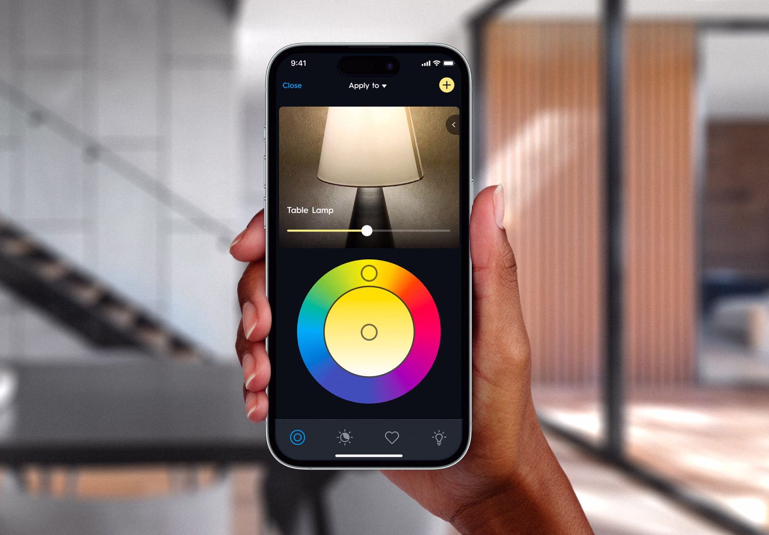 Hand holding a phone, using the Cync app color wheel to change a table lamp's light.
