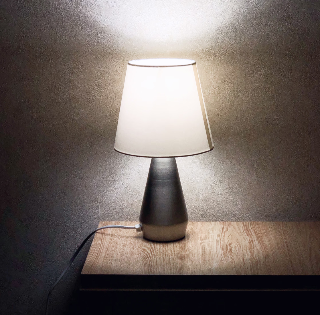 Lit table lamp on a wooden nightstand.