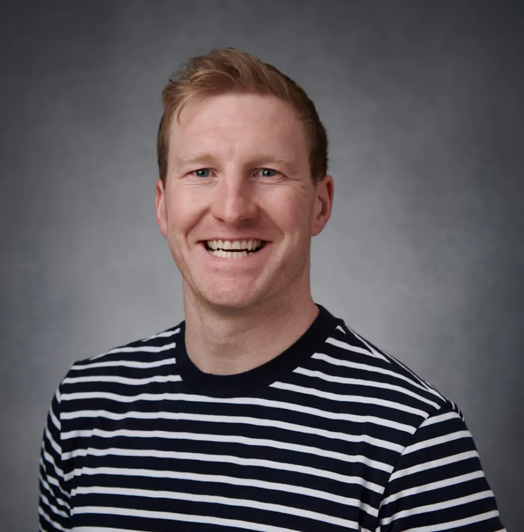 Smiling man with light hair wearing a black and white striped shirt against a gray background.