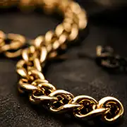 Close-up of polished yellow gold chain links on dark textured surface with warm lighting