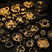 Assorted gold jewellery components and settings scattered on dark surface in warm lighting
