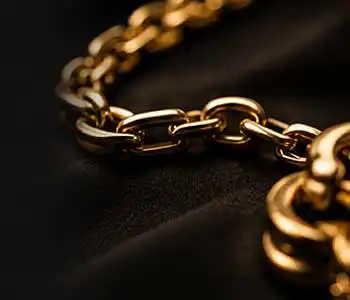 Close-up of a polished gold chain on dark fabric, highlighting interlocking links with warm lighting and shallow depth of field