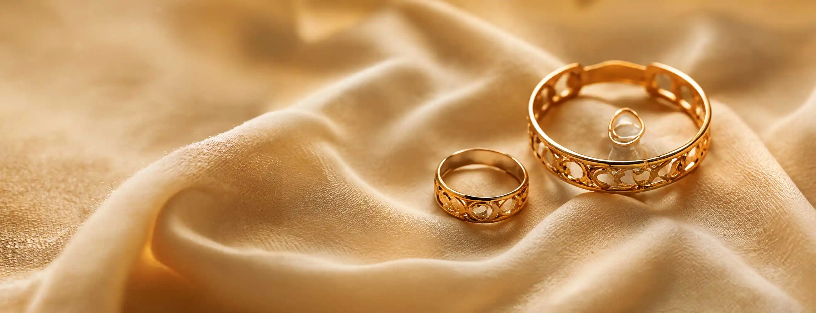 Gold plated bracelet and rings on soft fabric background with warm lighting, luxury jewellery close-up