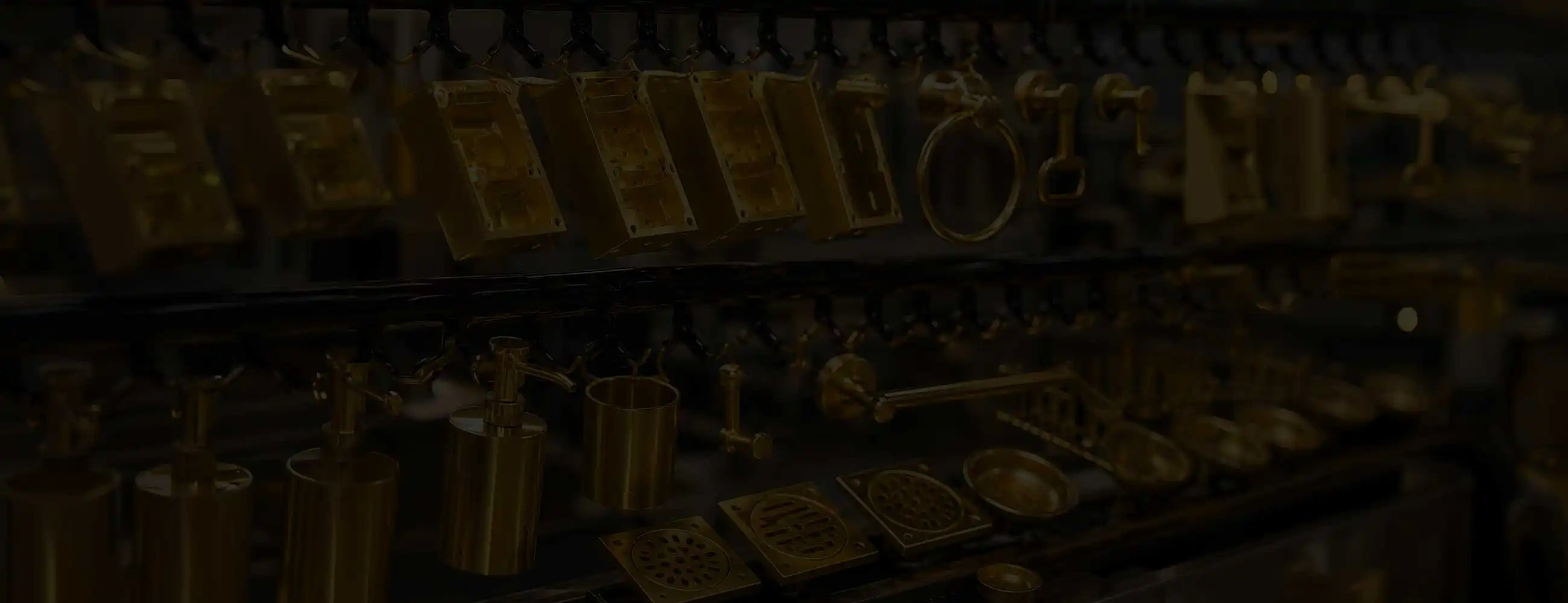 Gold-plated bathroom accessories and metal housings hanging on industrial rack, including towel ring, toilet paper holder, soap dispenser, and drain covers in polished gold finish