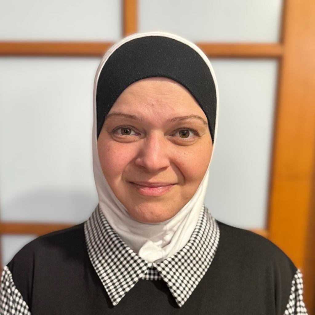 Woman wearing a black and white hijab and checkered collar smiling at the camera.