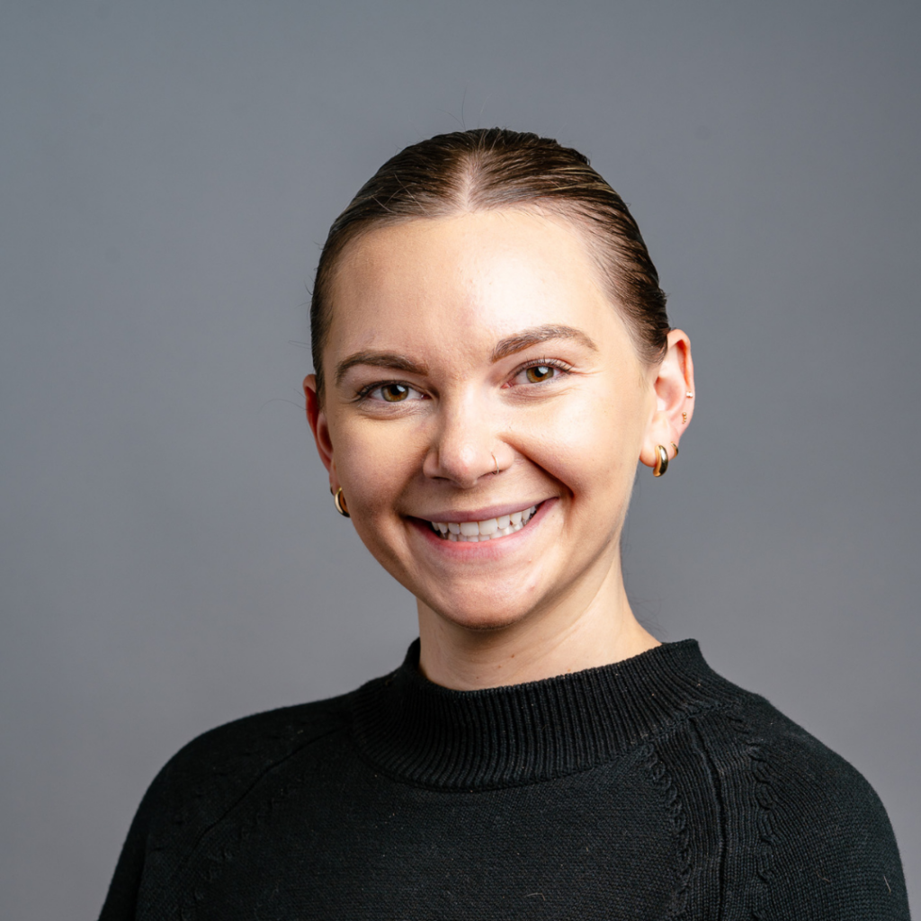 Smiling woman with slicked-back hair wearing a black sweater against a grey background.