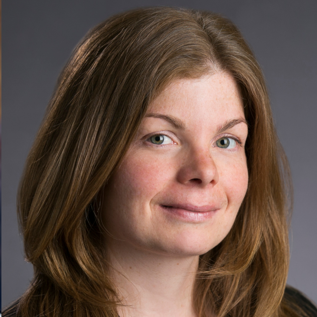 Close-up portrait of a woman with light brown hair and green eyes smiling slightly against a gray background.