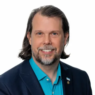 Smiling Martin Smith with medium-length hair and beard wearing a blue shirt and dark blazer.