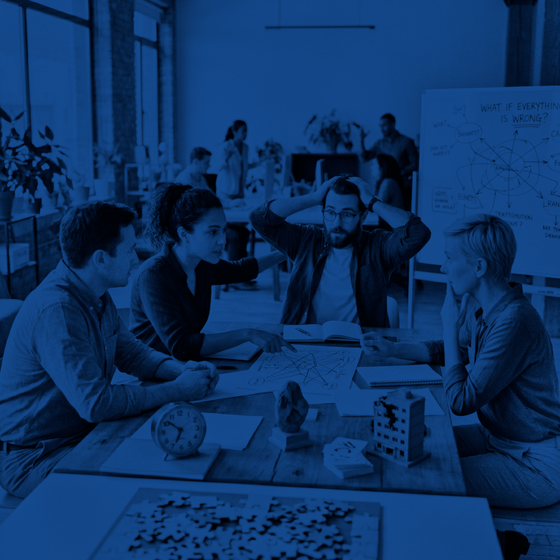 Four coworkers discussing ideas over diagrams and notes at a cluttered table in an office.