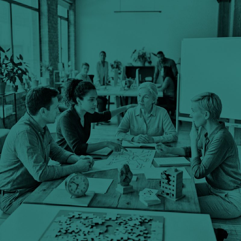 Four people actively discussing a diagram at a wooden table in a modern office space.
