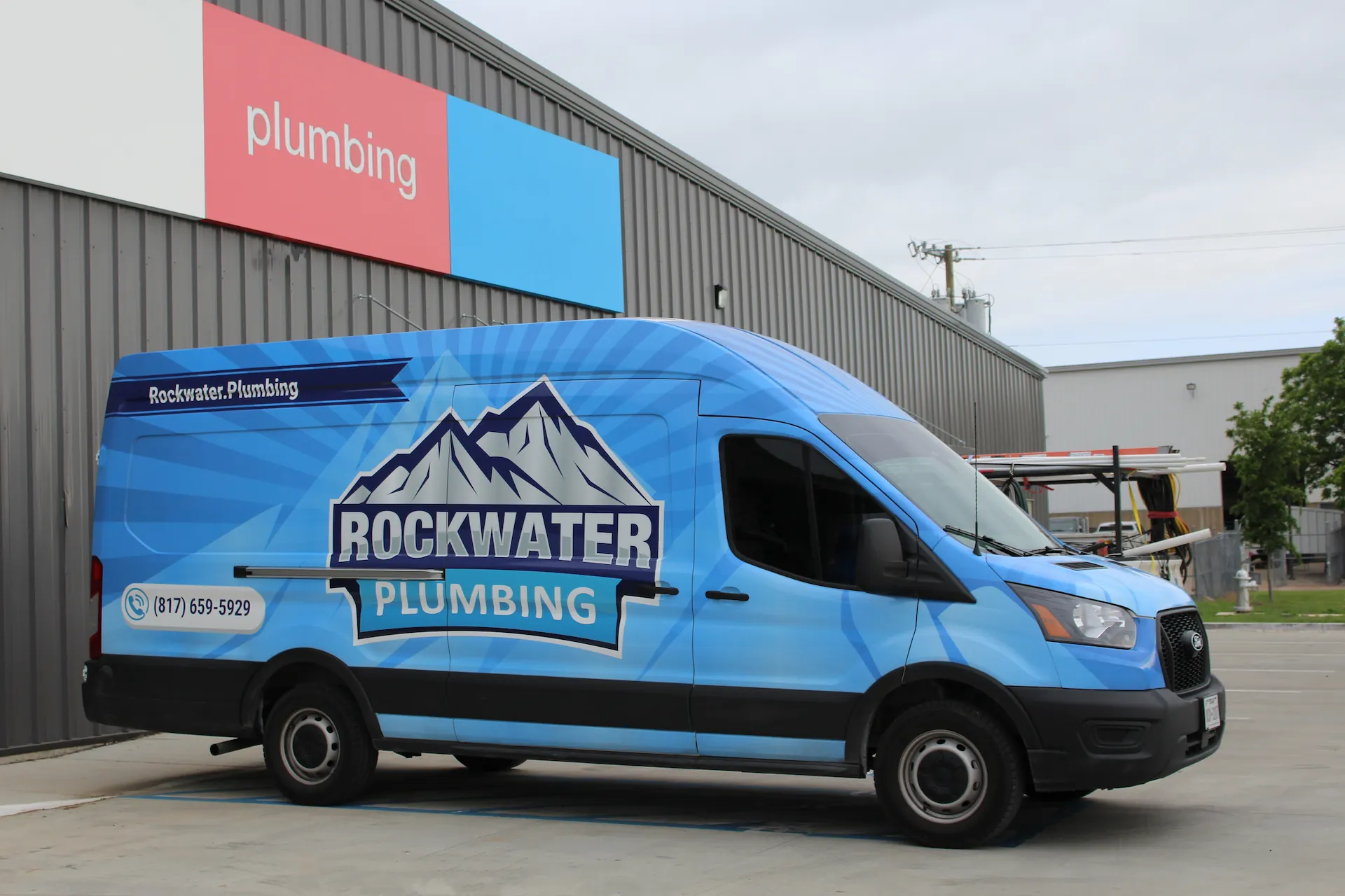 Blue Rockwater Plumbing van parked next to building with red and blue plumbing sign.