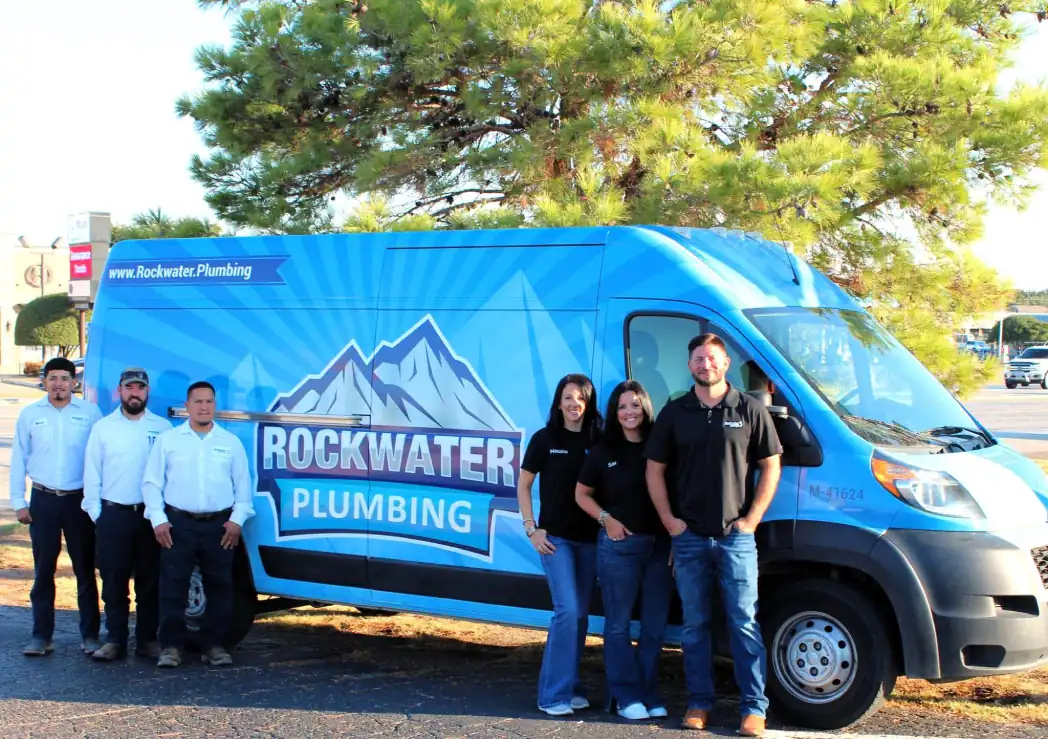Six Rockwater Plumbing team members standing beside a blue company van with logo.