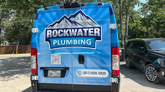 Back of blue Rockwater Plumbing van with mountain logo, phone number, and Texas license plate.