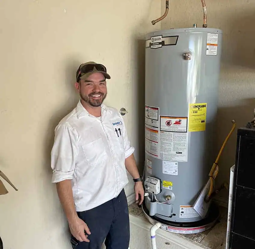 Technician smiling and standing next to a large gray water heater in a utility room.