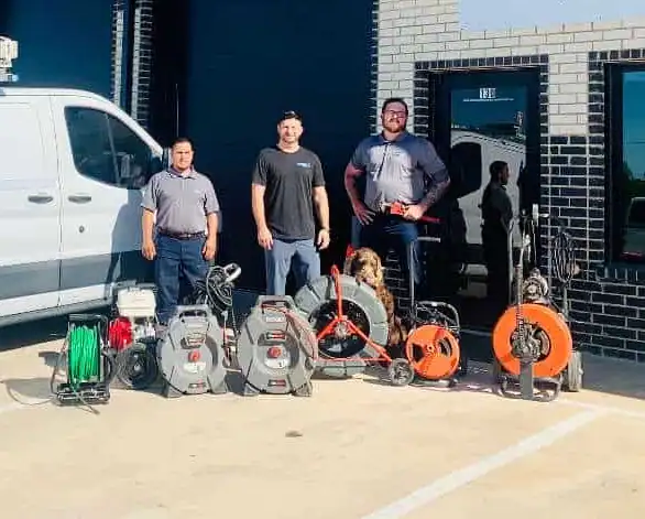 Three men standing outside near a white van with various plumbing or electrical cable equipment on the ground.