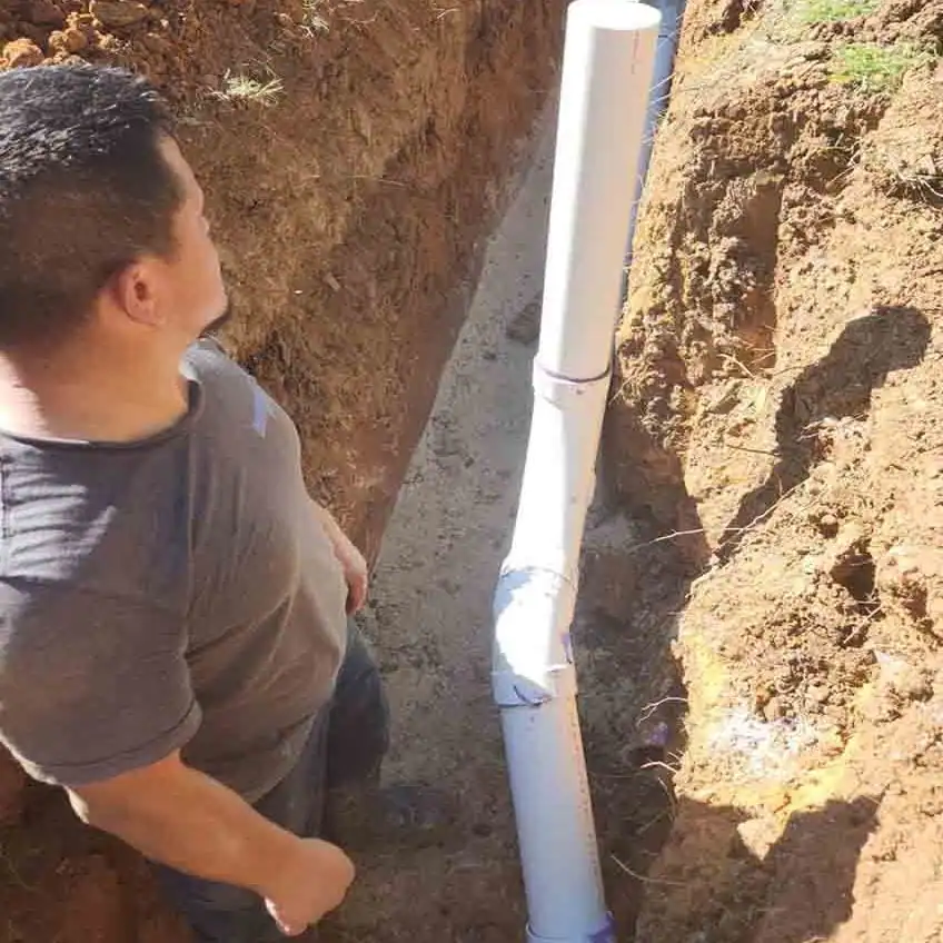 Man in a trench standing near a white PVC pipe installed underground for plumbing.