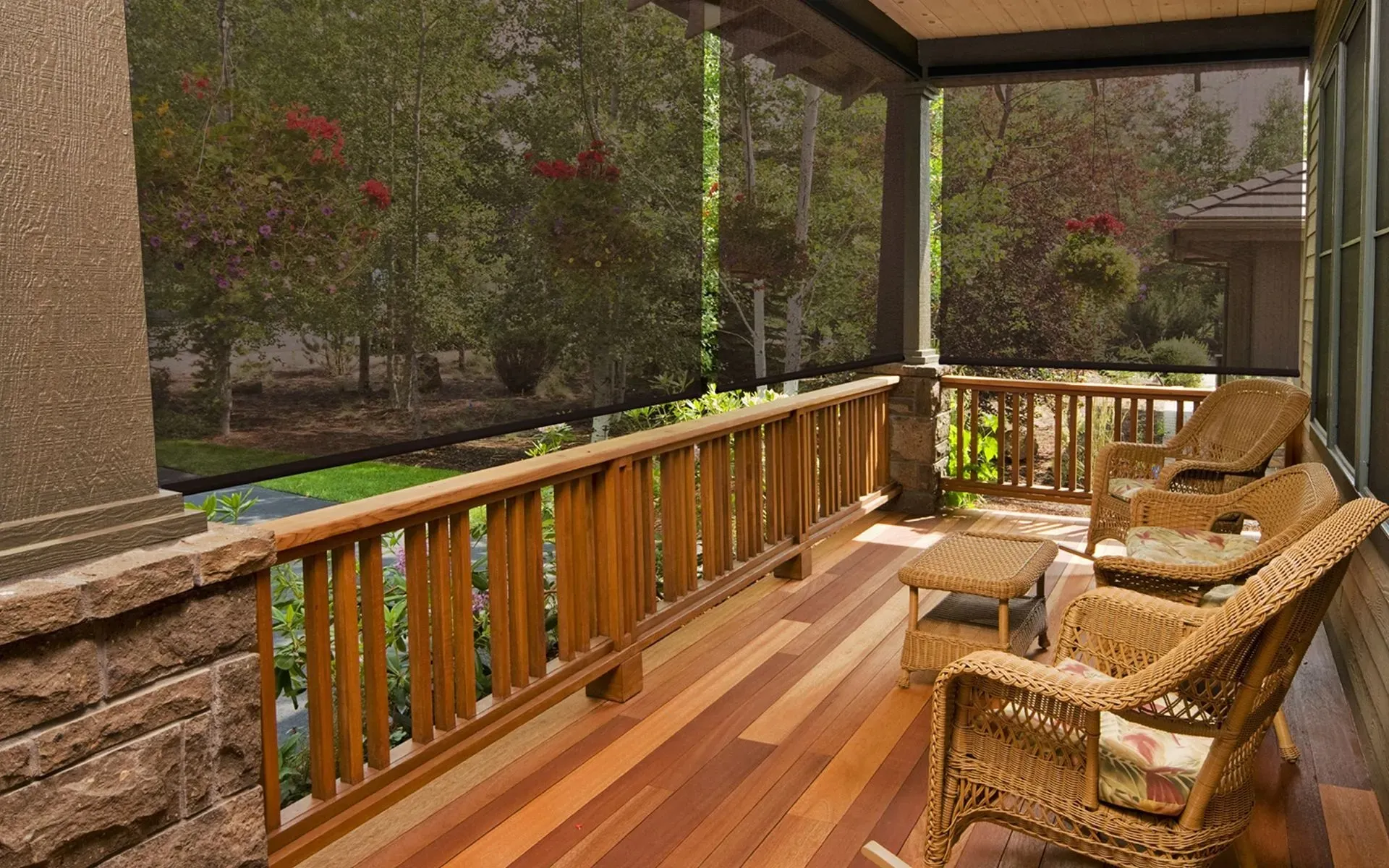 Exterior screen shades lowered around a covered wooden porch with wicker chairs