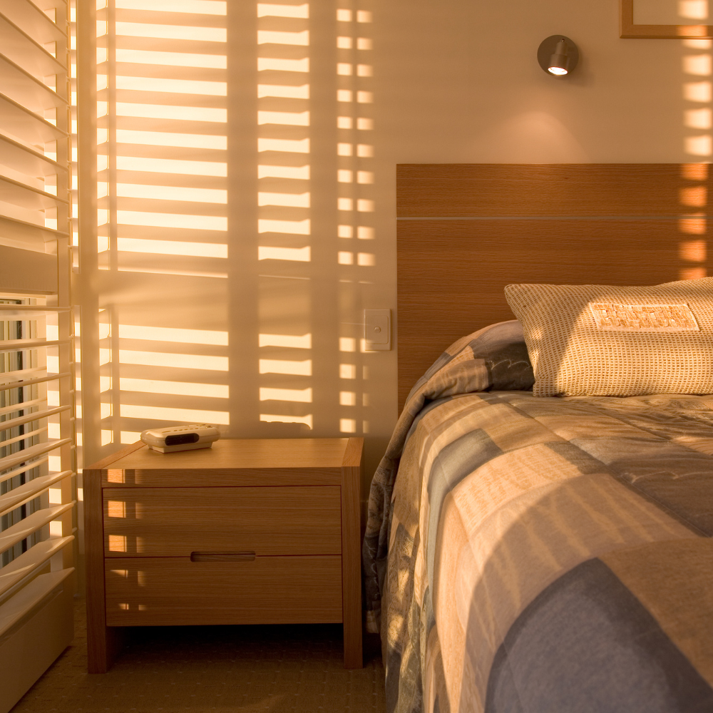 Warm sunlight through white plantation shutters casting stripes across a bedroom