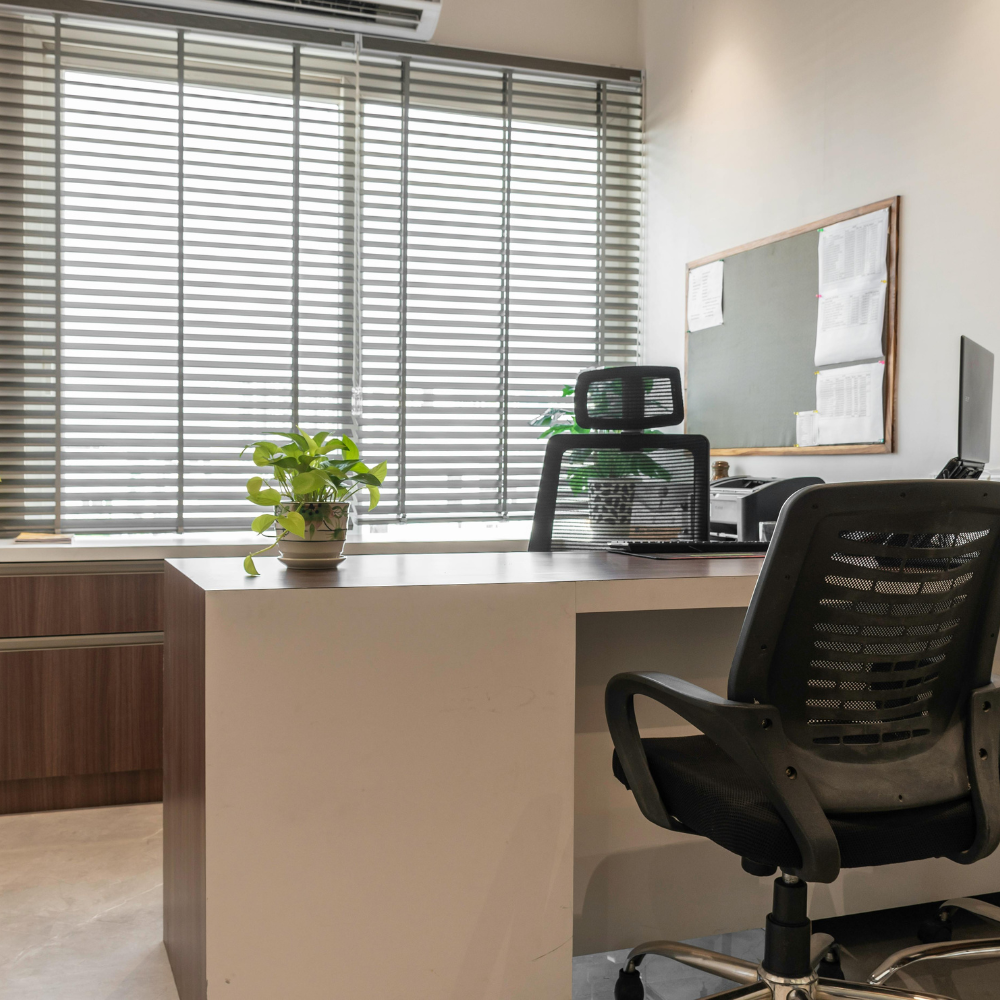 Gray horizontal blinds on a large window in a modern office with desk and mesh chairs