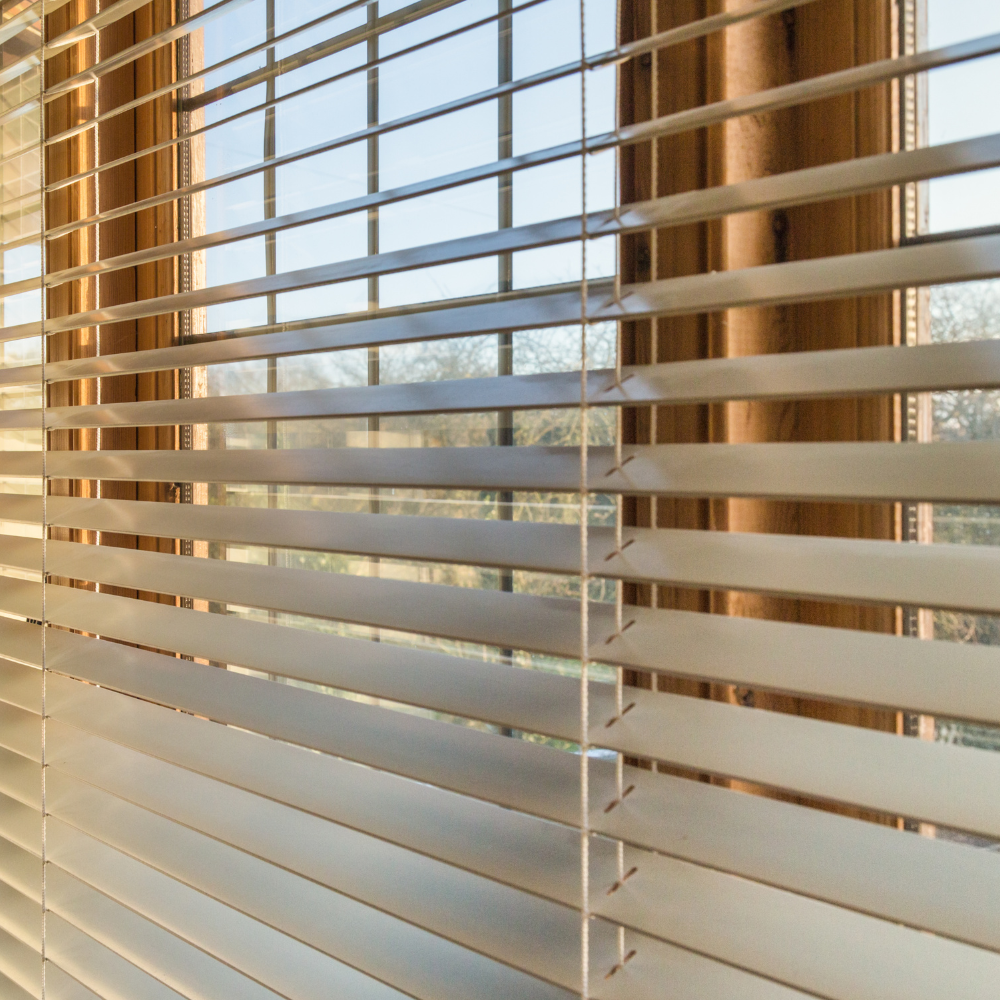 Close-up of white vinyl horizontal blinds tilted open on a sunny window