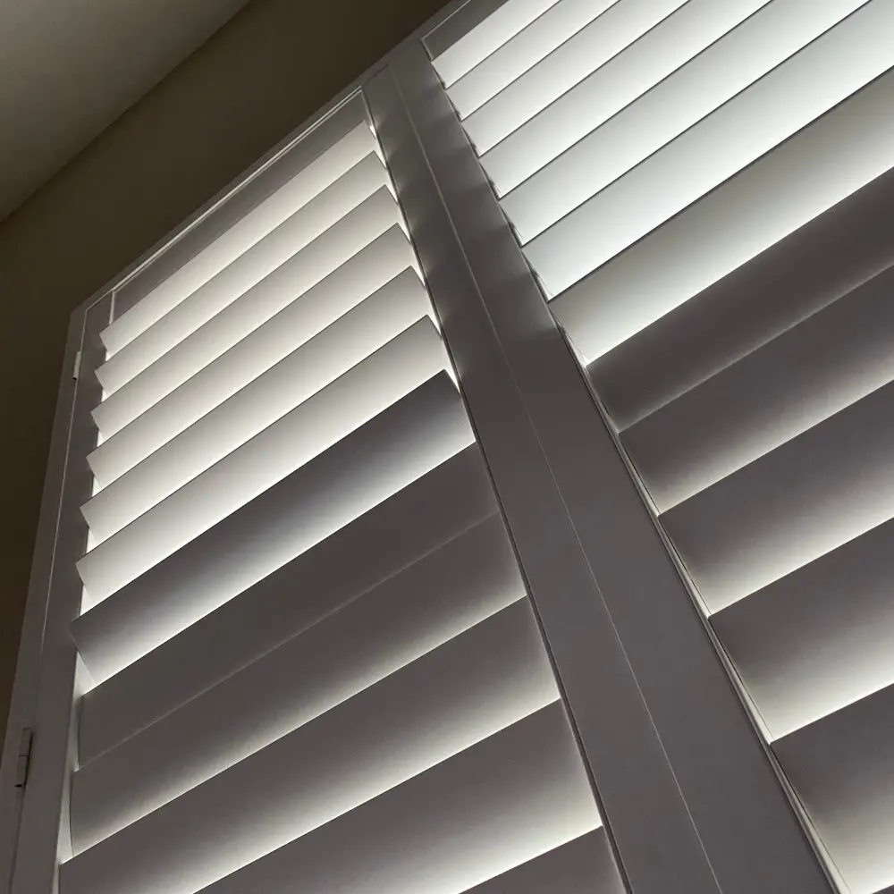 White plantation shutter louvers filtering daylight, viewed from below