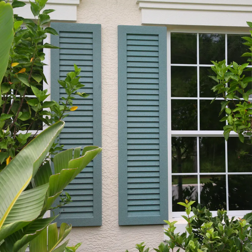 Teal louvered exterior shutters beside a white-framed window on a stucco home