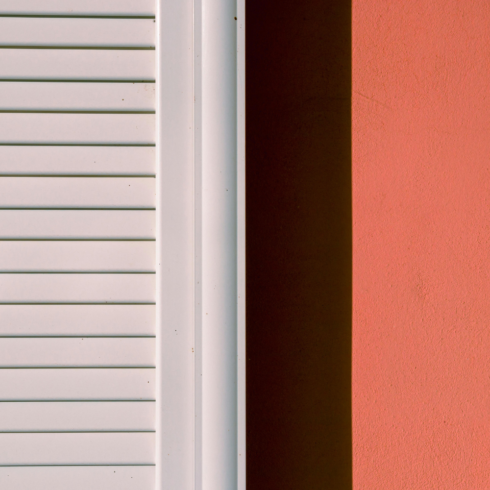 Close-up of a white louvered shutter beside a coral stucco wall