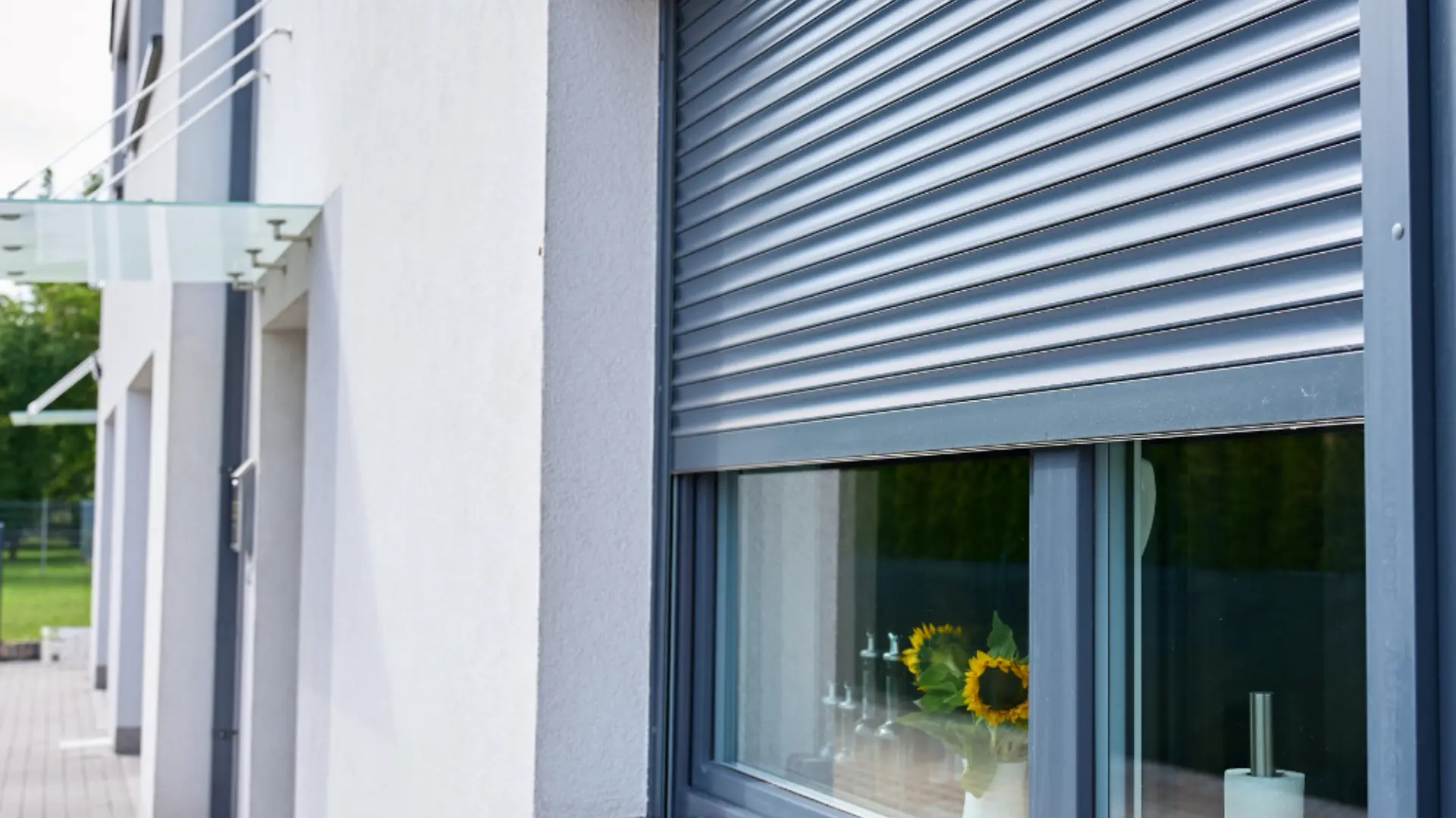 Exterior rolling security shutter partly lowered over a home window, after installation