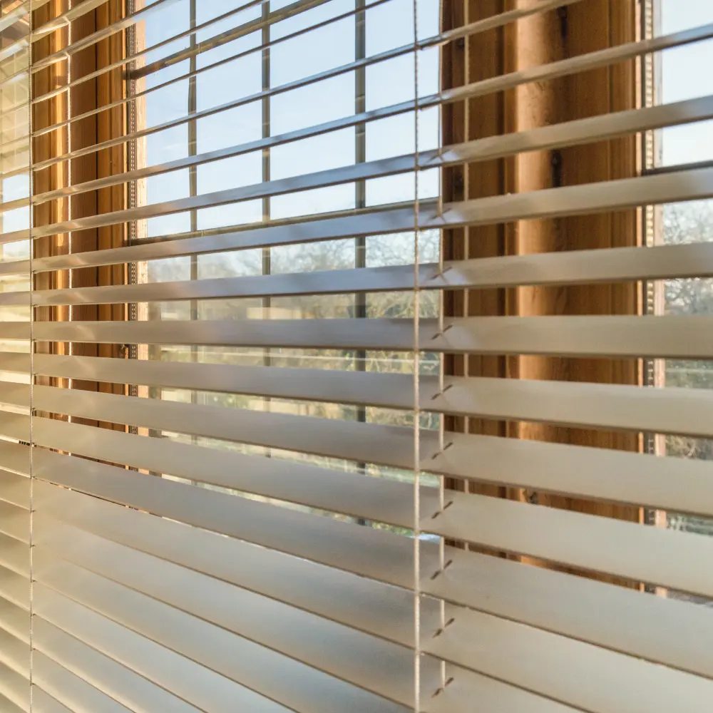 Close-up of white vinyl horizontal blinds tilted open on a sunny window