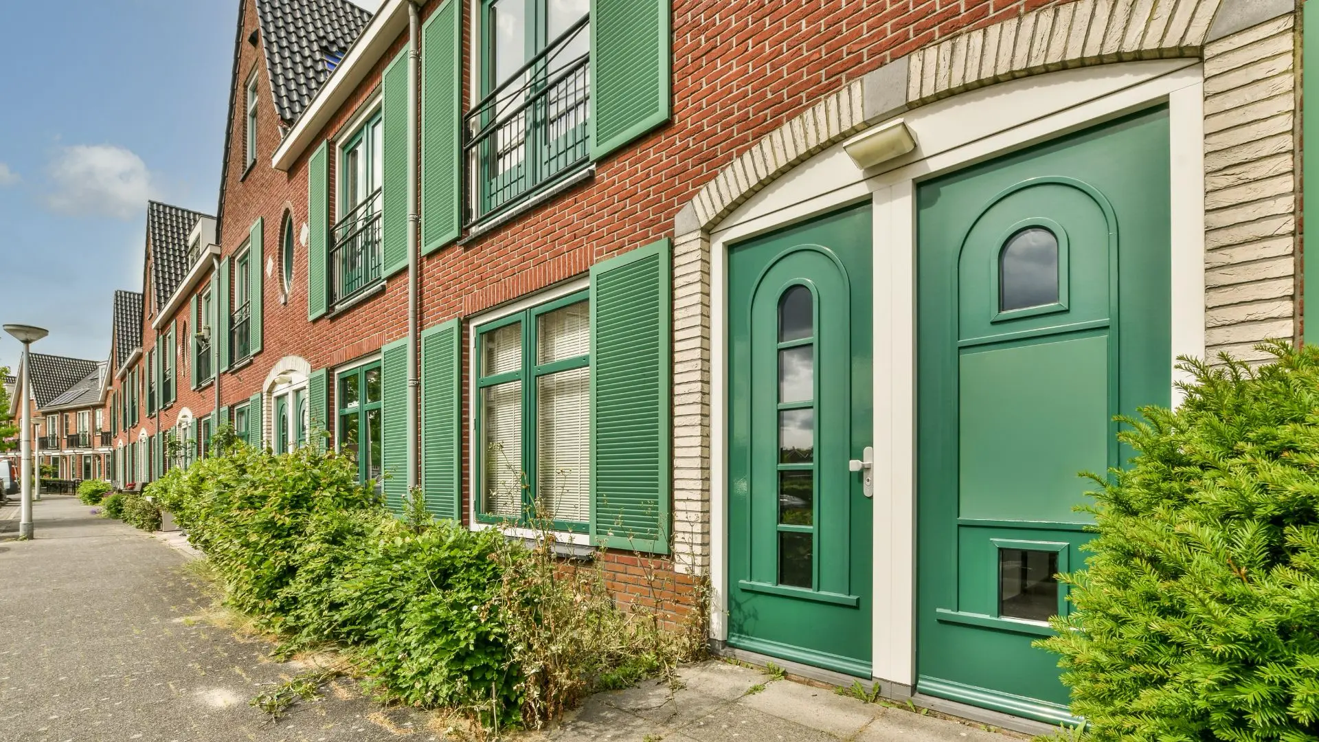 Green exterior window shutters on a brick row house with matching green front doors