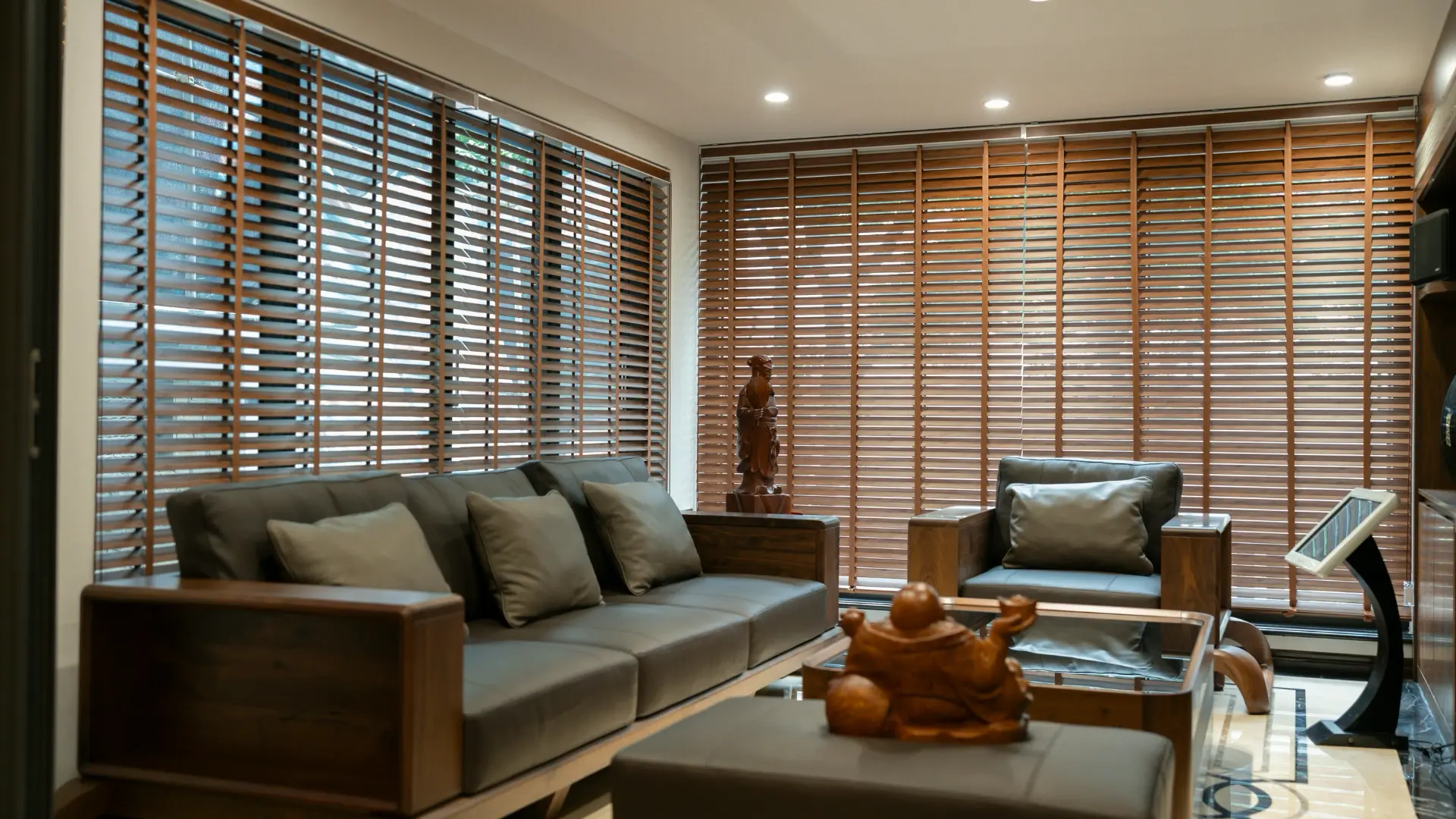 Living room with wood blinds across a wall of windows behind a sofa and armchair