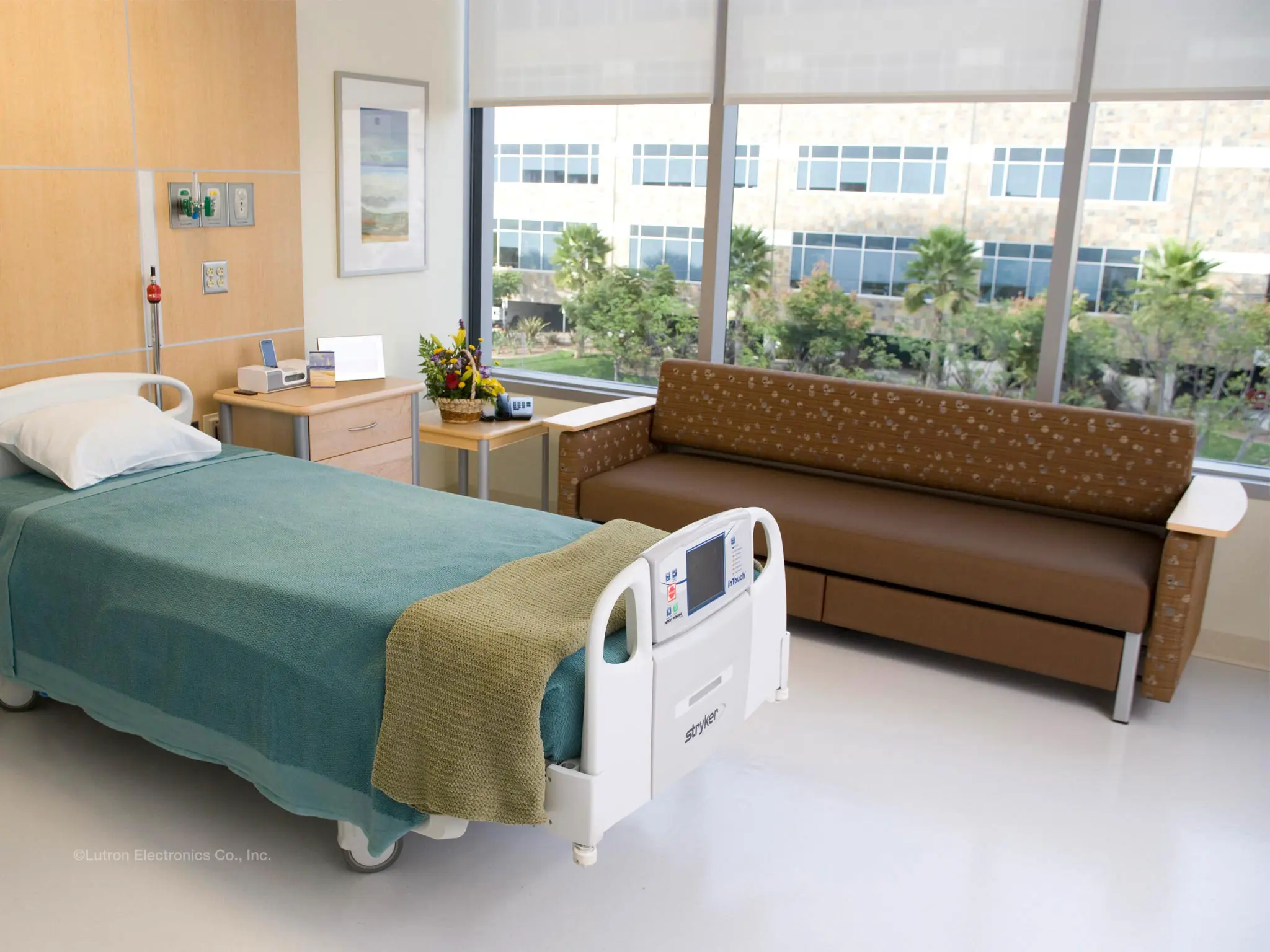Hospital patient room with roller shades raised above large windows